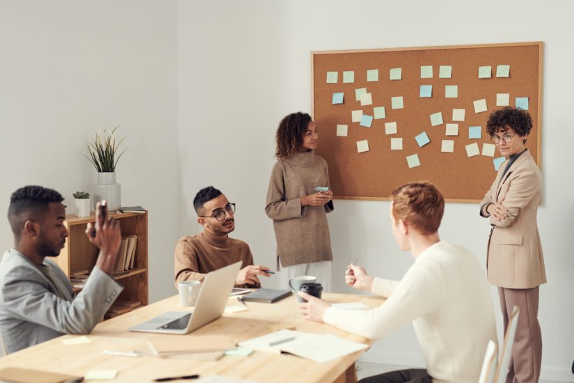 Squad formada por 5 pessoas conversando em frente a um quadro de post its