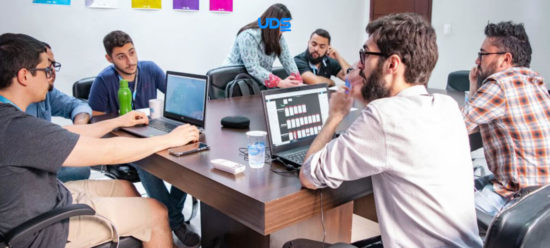 alt="dois homens e uma mulher conversam enquanto olham para as telas de seus notebooks em uma fábrica de software"›
