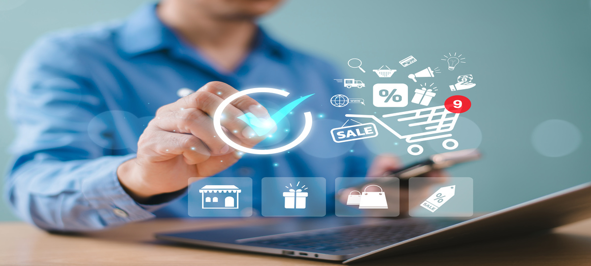 Homem vestindo camisa azul em desfoque clica em símbolos em destaque que remetem ao uso de cloud no varejo, assim como outras tecnologias relacionadas. Há um símbolo de carrinho à frente da imagem, indicando o contexto de compras online..