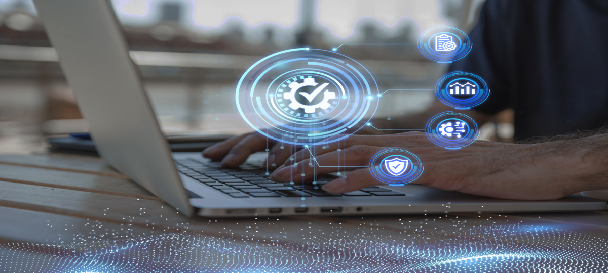 Mãos humanas digitam em notebook prateado em foco. À frente da imagem, símbolos em tons azulados se conectam em esferas pequenas, à uma esfera central que contém o símbolo de engrenagem com um “check” ao meio, simbolizando a integração de sistemas.