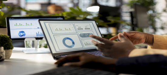 mãos humanas trabalhando num notebook que exibe uma plataforma de dados e gráficos relacionados a eles
