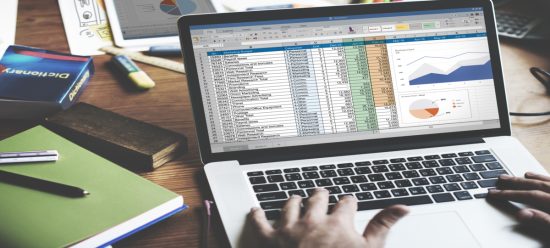 maos humanas digitam em laptop cinza claro com tela focada em planilhas e gráficos de dados, simbolizando uma consultoria de bi