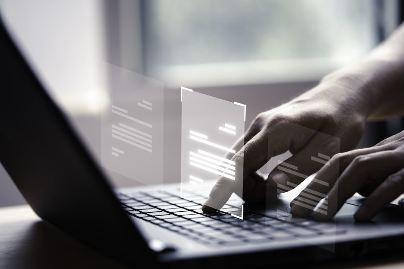 mãos humanas que digitam sobre laptop cinza. Acima da máquina está um elemento gráfico que represanta códigos de IA, representando a atuação de prompt injection