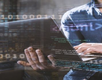 homem digitando em notebook com símbolos html e css à frente da imagem, simbologia para engenharia de dados
