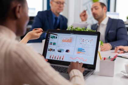 time de master data manegement discutindo ao redor de uma mesa de reunião, com notebook aberto sobre ela demonstrando gráficos de dados a serem gerenciados