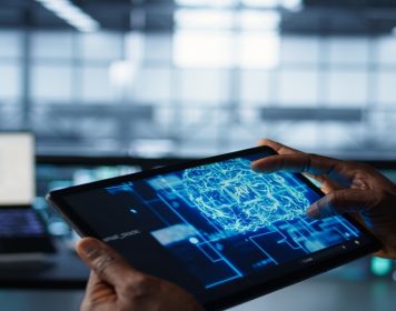 tablet segurando por mãos humanas com tela mostrando elemrntos relaiconados à automação inteligente em cores azuis