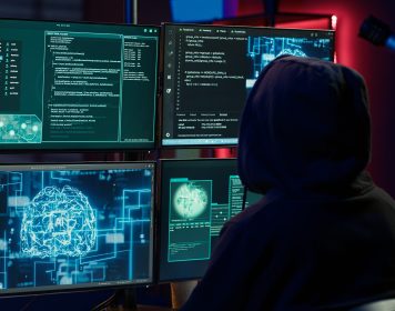 homem vestindo capuz preto mexendo em computadores, o que representa os ataques protegidos pelo hardening