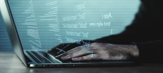 mãos humanas digitando códigos de recodificação em notebook que é cinza e está de costas na imagem. à frente da tela, saem, em branco, códigos de recodificação.