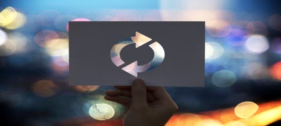 mão humana segurando papel com recorte vazado em formato de "refação", sugerindo o refatoring trabalhando ao longo do conteúdo; Ao fundo, há em desfoque luzes coloridas vindas de máquinas como computadores, o que relaciona a imagem à tecnologia.